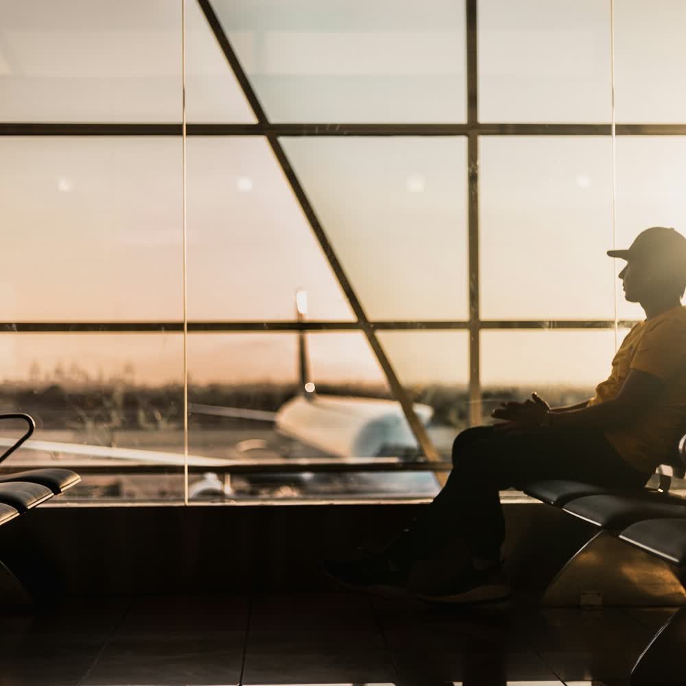 A lone traveller waiting in a departure lounge at golden hour, unhurried.