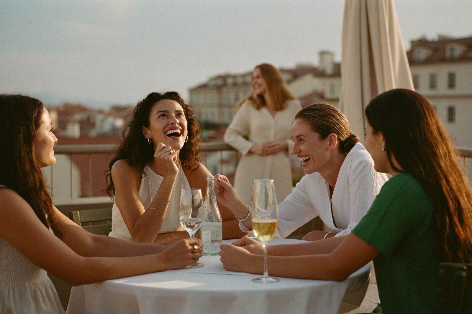 Four women laughing together at a rooftop table at golden hour on the first evening of a trip.