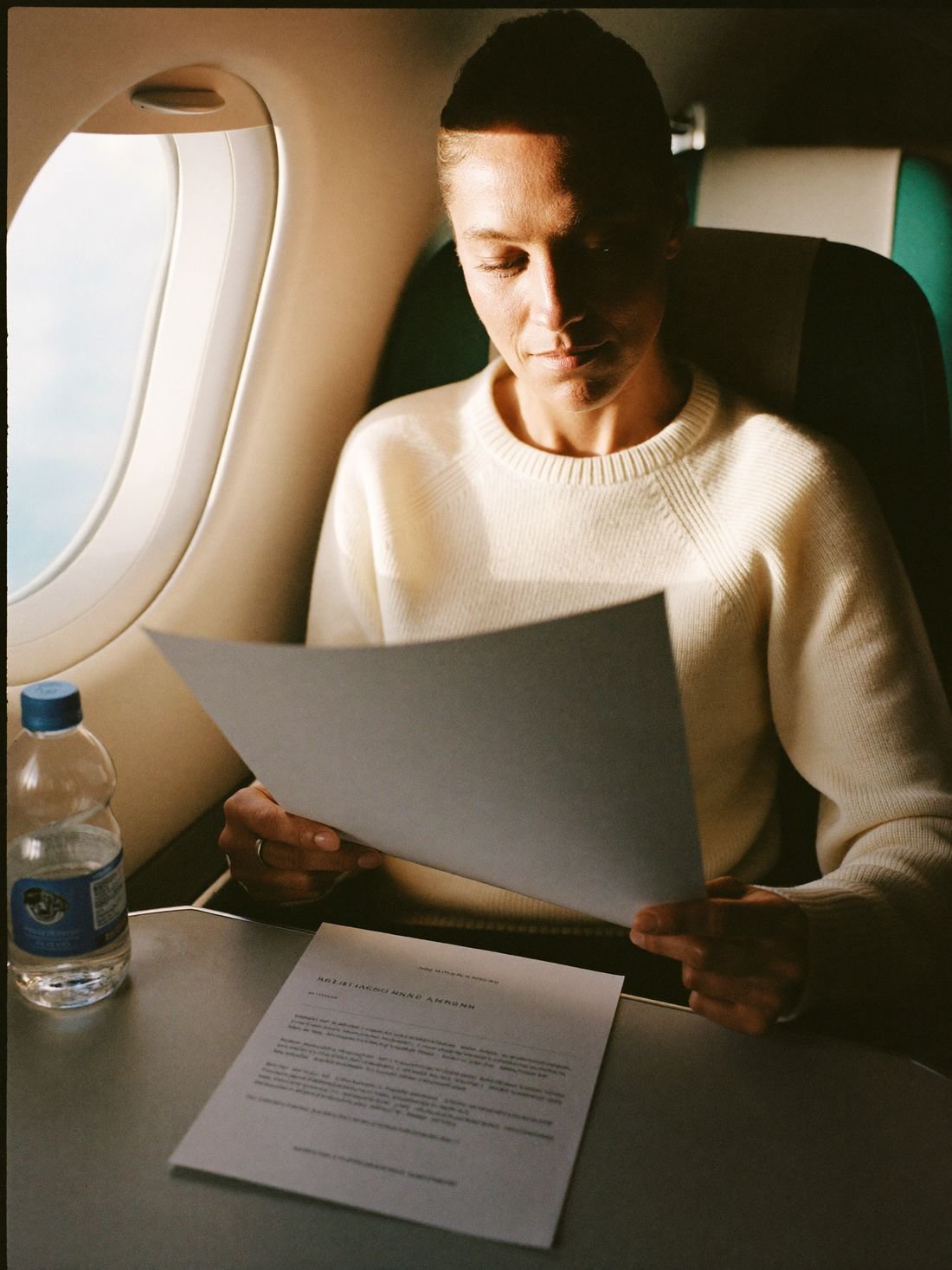 A woman in a window seat at sunrise reading a one-page reference sheet, calm and awake.